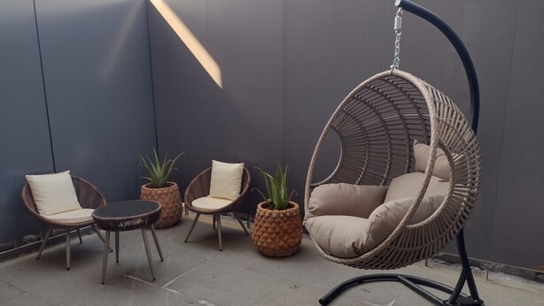 A patio area with wicker furniture, including a hanging chair, two chairs, and a small table.