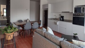 A modern kitchen with white cabinets, a black refrigerator, and a microwave. There is a dining area with a table and chairs, and a gray sofa in the living area.