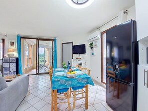 Un comedor con una mesa dispuesta para cuatro personas, un refrigerador negro grande y un televisor montado en la pared.