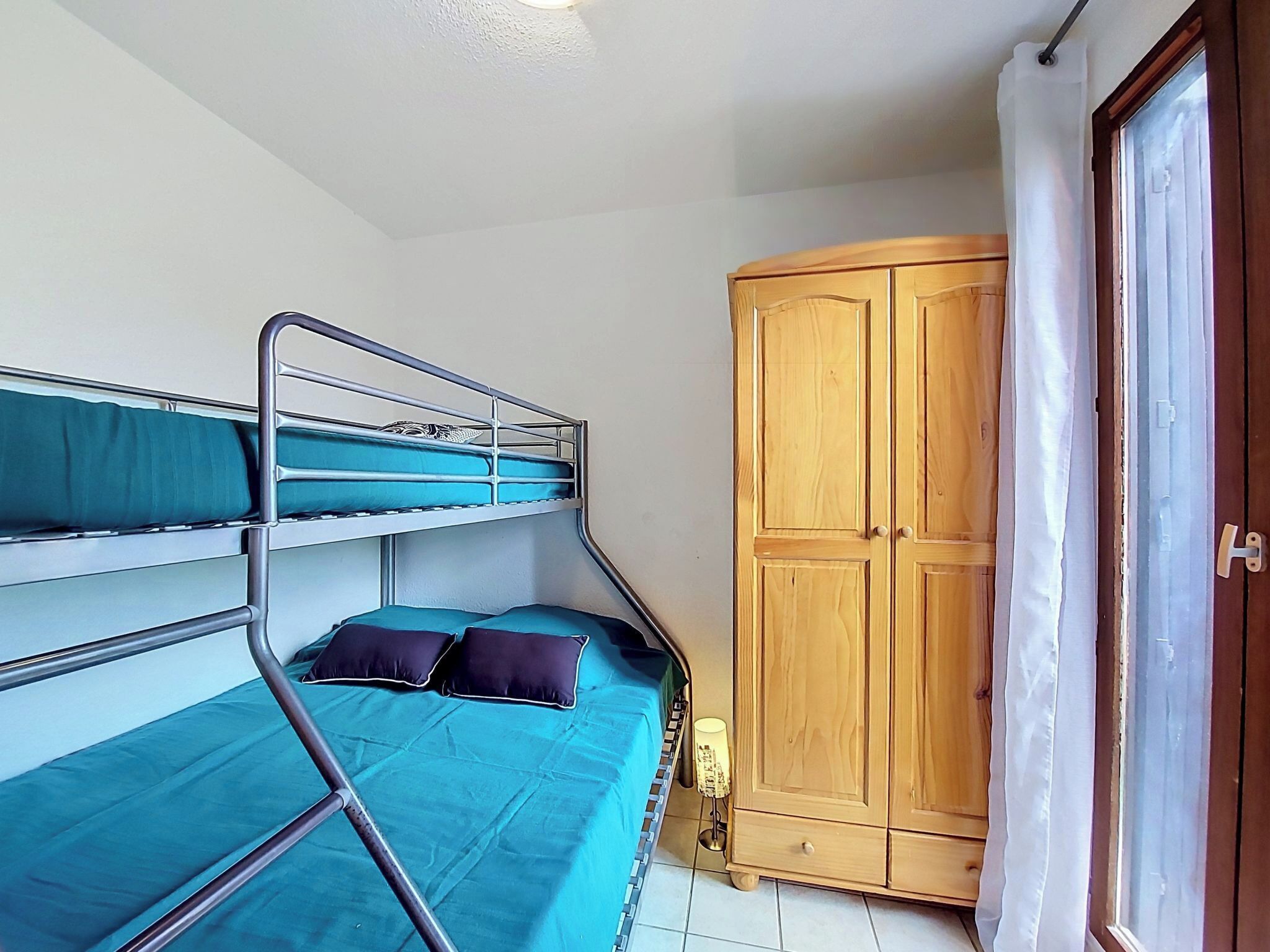 Ein Etagenbett mit blauer Bettwäsche, ein Holzschrank und ein Fenster mit Vorhängen.