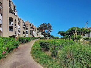 A pathway leading to a multi-story building with balconies, surrounded by well-maintained greenery and trees. - Dominica by Interhome (Le Barcarès)