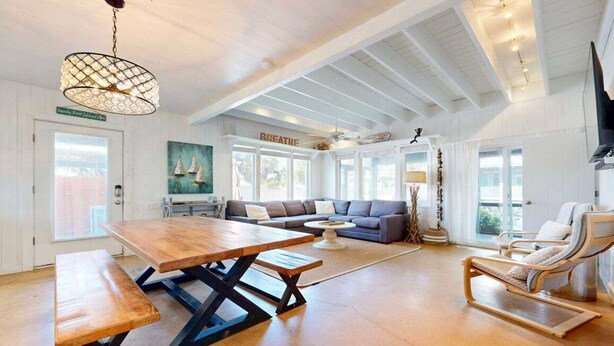 Amplia sala de estar con una mesa de madera, un sofá y una silla. Un ventanal grande ofrece luz natural y vistas al exterior.
