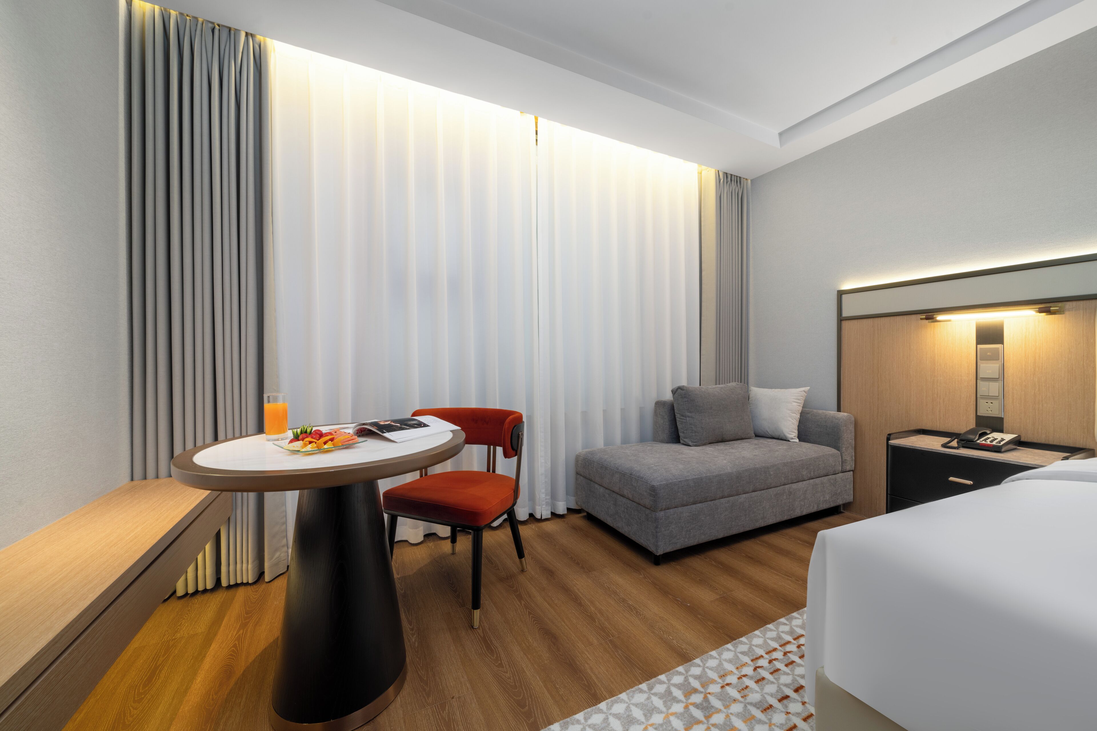 Une chambre d’hôtel moderne avec une table ronde, deux chaises, un canapé, un lit et une table de chevet avec une lampe.