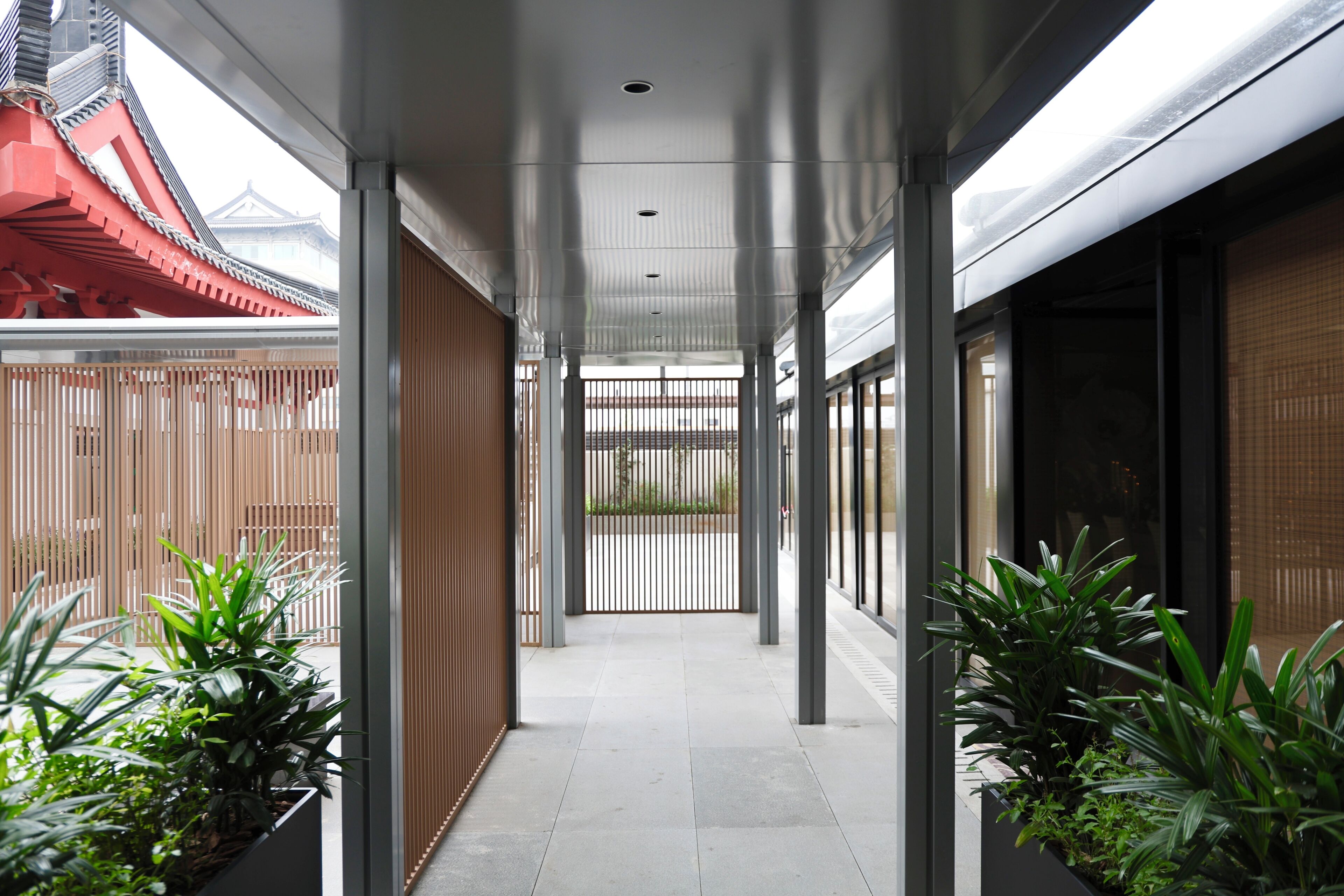 A corridor with a modern design, featuring a wooden fence on one side and a glass wall on the other.
