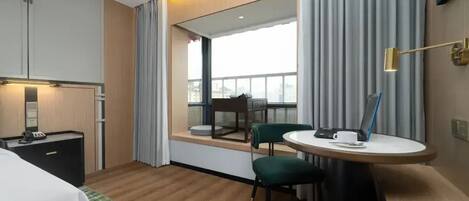 Habitación de hotel con cama, escritorio con computadora portátil, silla, mesita pequeña y ventana con cortinas.