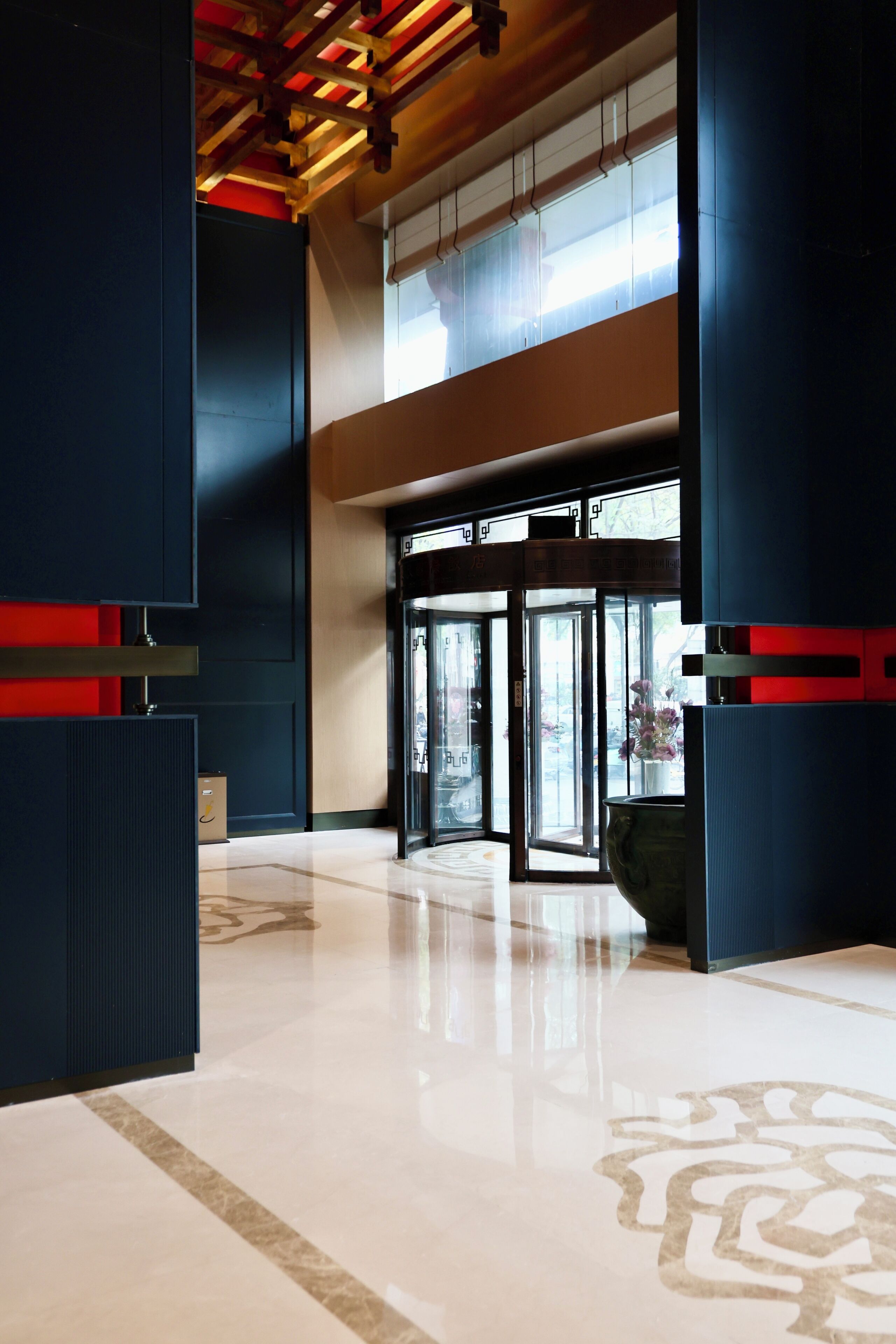 A spacious lobby with a polished floor, a large entrance with glass doors, and a high ceiling with wooden beams.