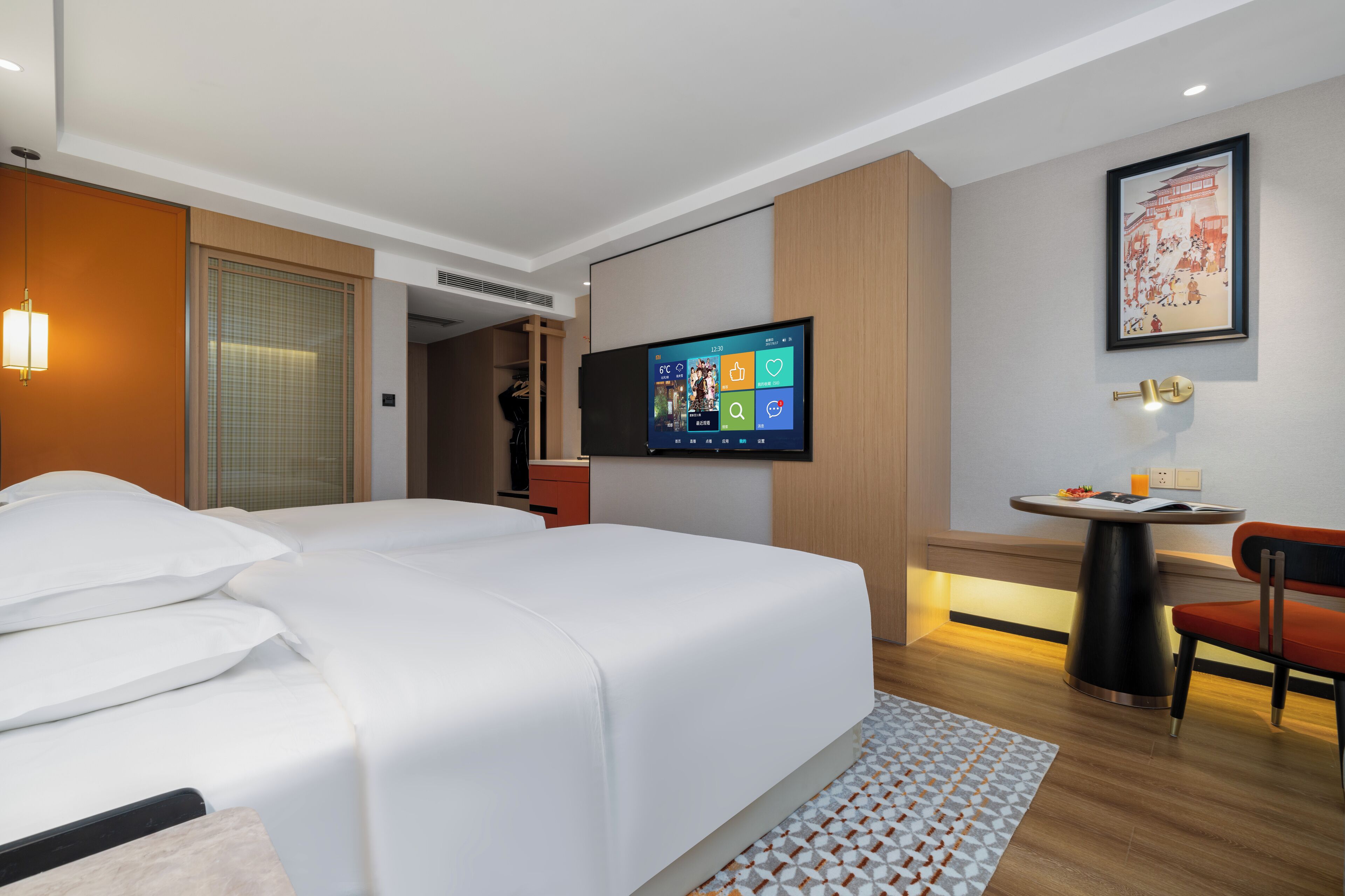 Habitación de hotel con cama, televisión en la pared, una mesita con silla y un cuadro enmarcado.