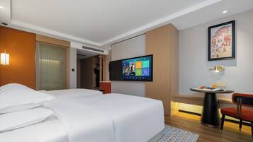 Habitación de hotel con cama, televisión en la pared, una mesita con silla y un cuadro enmarcado.
