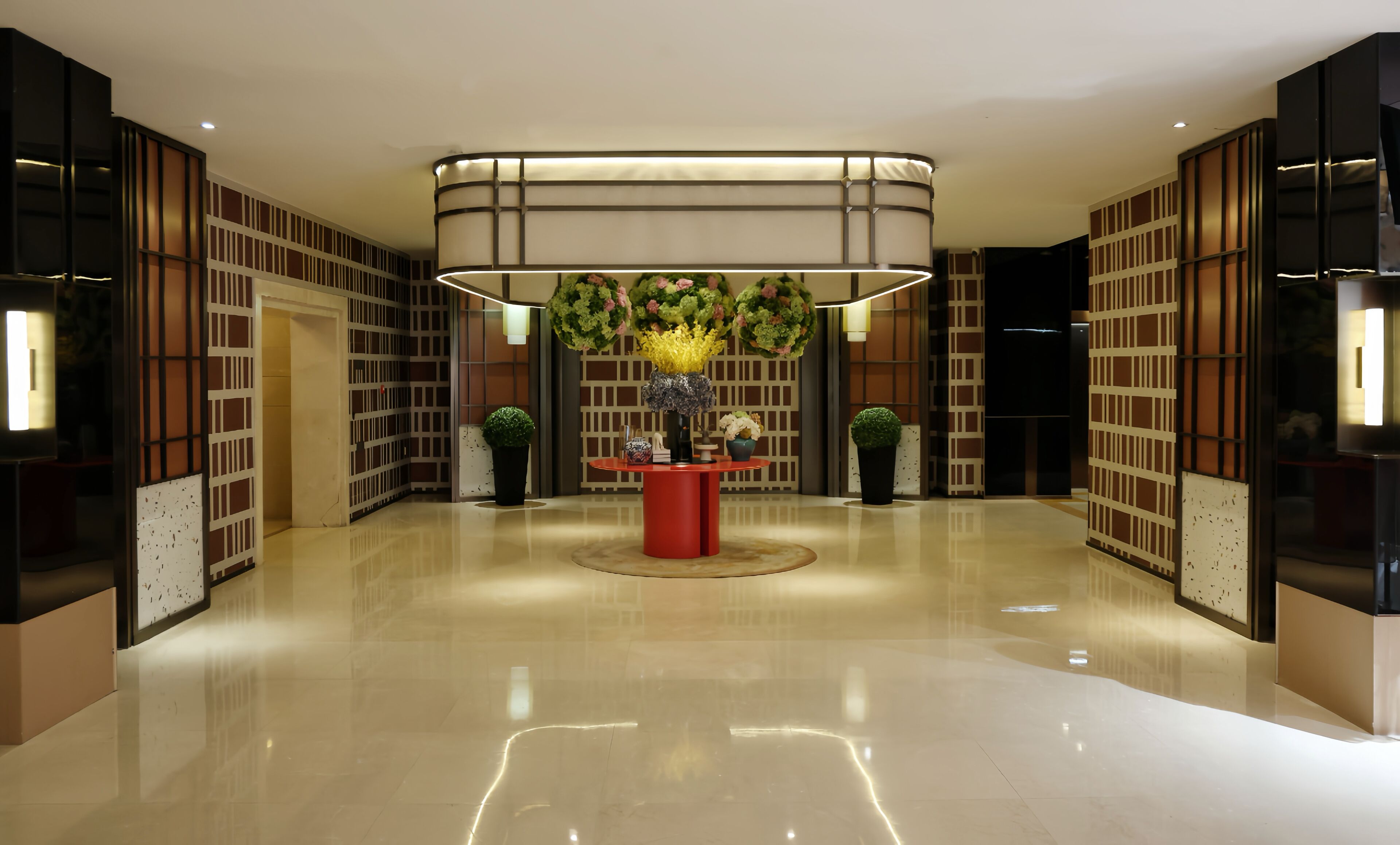 Un moderno vestíbulo con una mesa roja central, rodeada de estanterías y plantas decorativas.