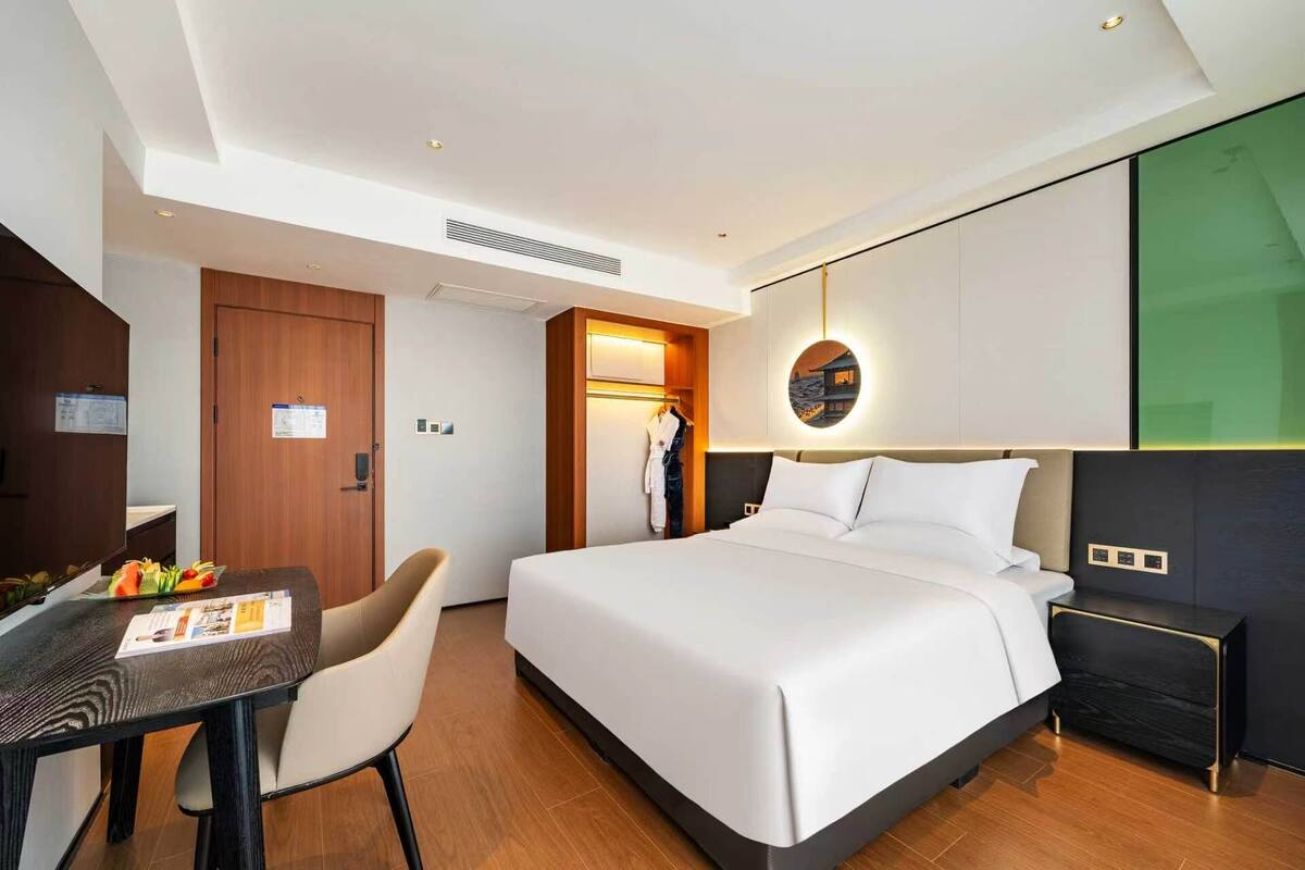 A hotel room with a bed, bedside table, chair, and a desk with a menu.