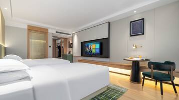 A modern hotel room with a large bed, a desk with a chair, a flat-screen TV mounted on the wall, and a framed picture above the TV.