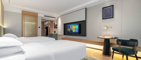 A modern hotel room with a large bed, a desk with a chair, a flat-screen TV mounted on the wall, and a framed picture above the TV.