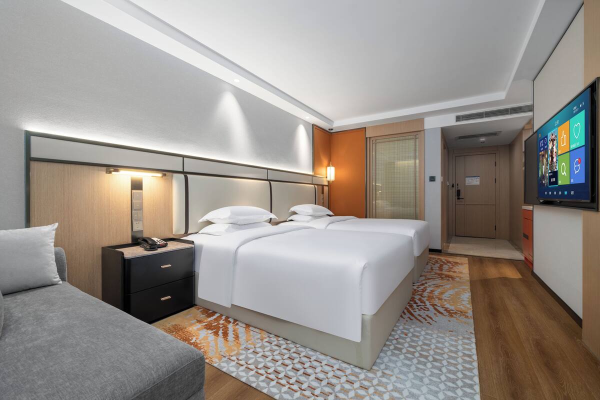 A modern hotel room with a large bed, bedside tables, a desk, and a flat-screen TV.