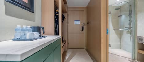A hotel bathroom with a shower, a sink, and a mirror. There is a towel rack and a door with a sign on it.