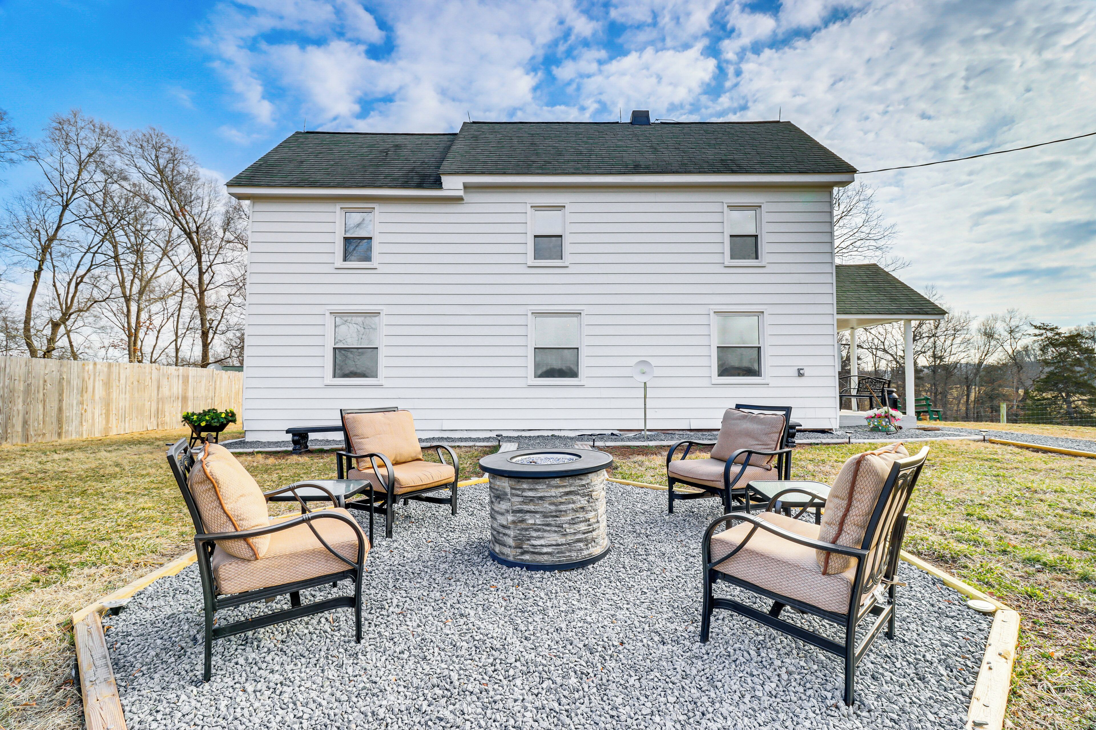 A white house with a covered porch, a gravel patio with four chairs and a round table, and a wooden fence in the background.