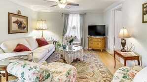A living room with a sofa, floral armchairs, a coffee table, a television, and a ceiling fan. - Fire Pits, Creek View: Historic Virginia Farmhouse (Bealeton)