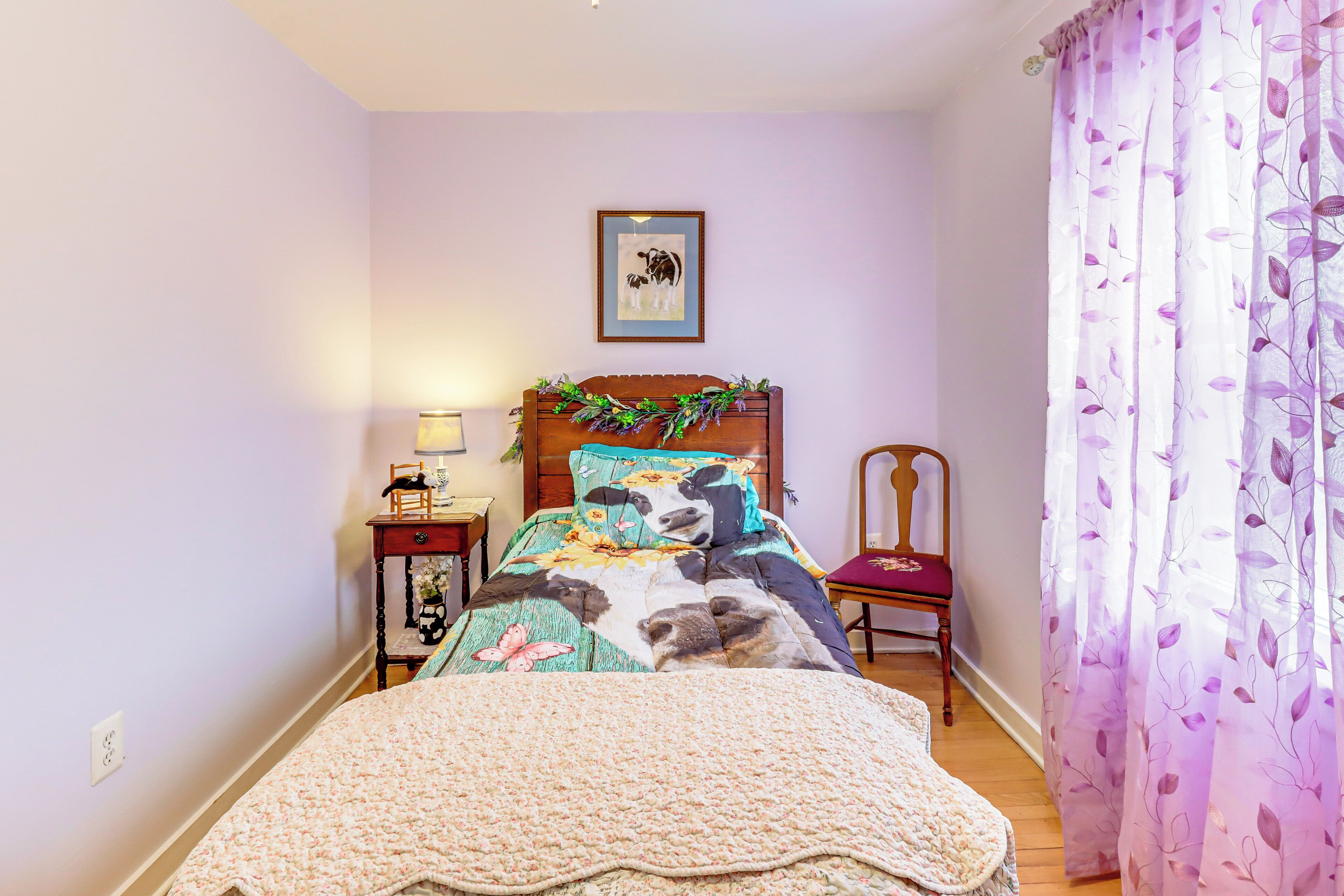 Una camera da letto con un letto, una sedia, un comodino, una lampada e un quadro appeso al muro.