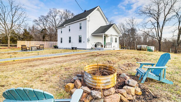 A white house with a front porch, a fire pit, and two Adirondack chairs. - Fire Pits, Creek View: Historic Virginia Farmhouse (Bealeton)