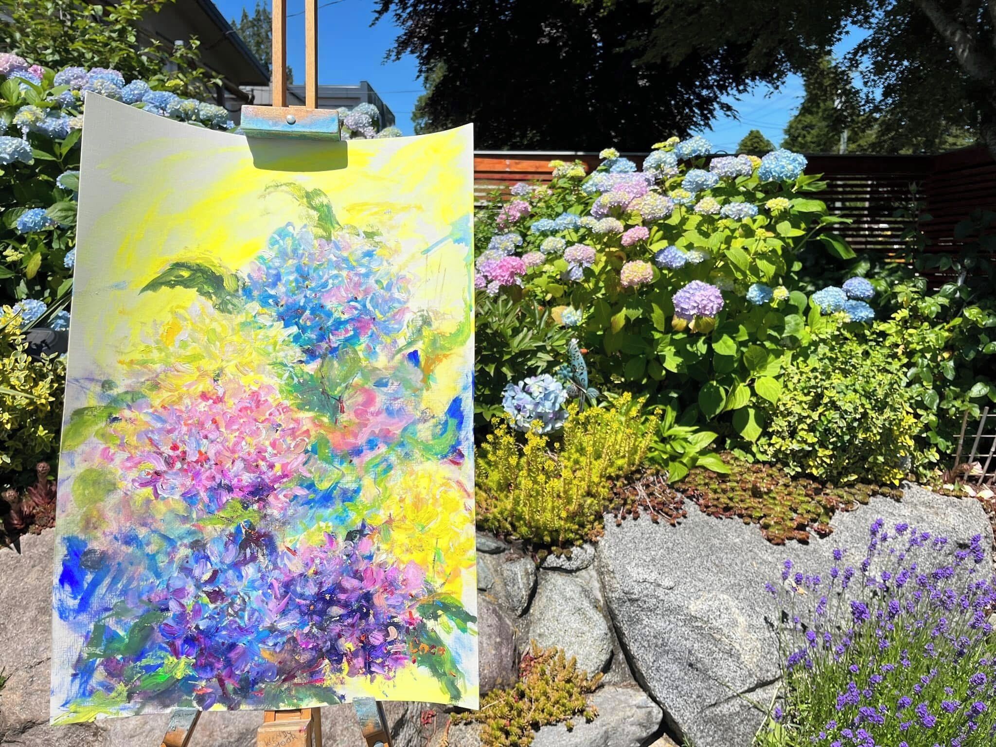 Ein Gemälde mit Blumen auf einem Malkasten, im Hintergrund ein Garten.