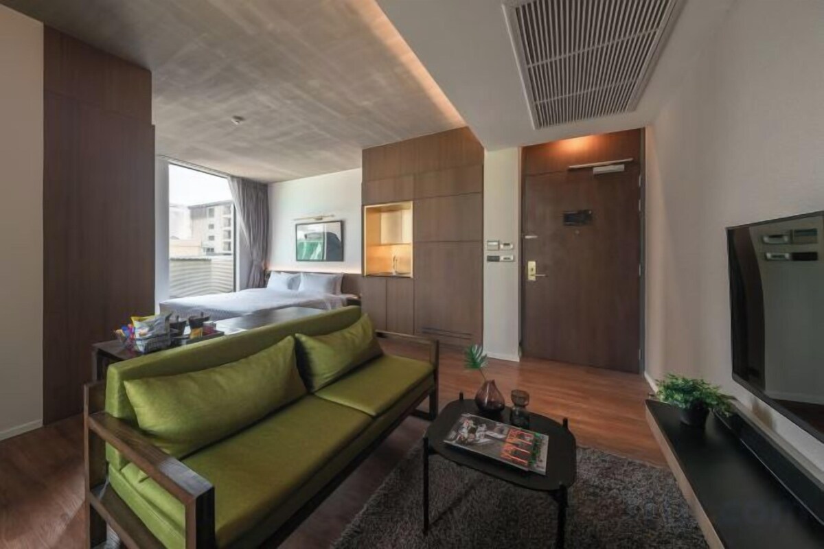 A modern hotel room with a green sofa, a bed, a TV, and a small table.