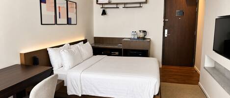 Ein Hotelzimmer mit Bett, Nachttisch, Sessel, Schreibtisch und Fernseher.