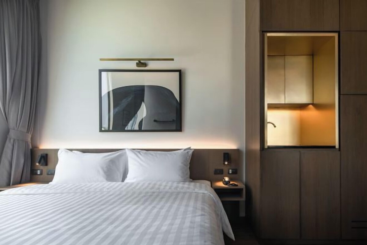 A hotel room with a bed, a nightstand, a wall-mounted light, a framed picture, and a built-in cabinet.