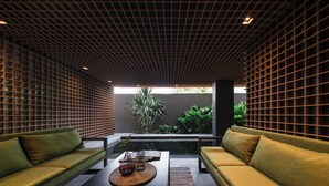 Un interior moderno con techo de diseño de cuadrícula, dos sofás verdes, una mesa de centro y una pequeña fuente de agua.
