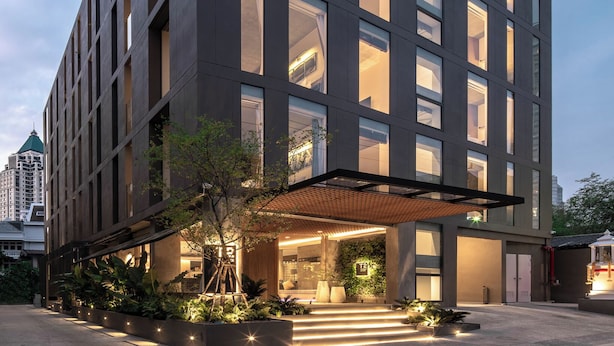 Un edificio moderno con amplios ventanales, un acceso cubierto y un área ajardinada con plantas.