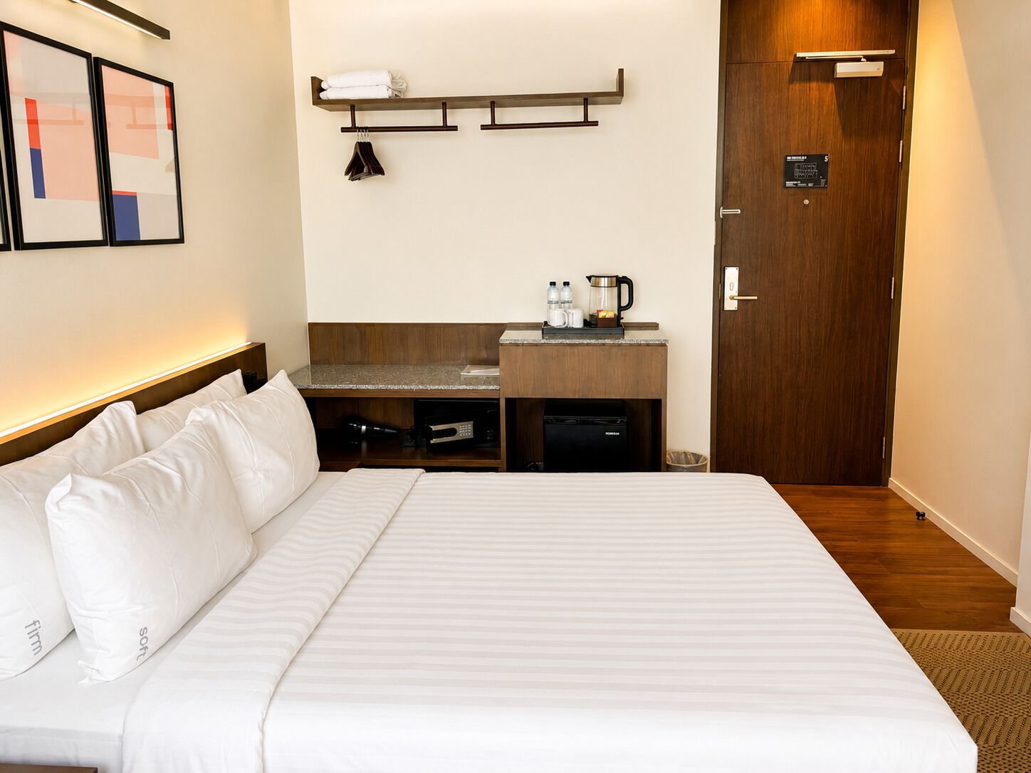 A hotel room with a large bed, a desk with a coffee maker, and a door with a room number sign.