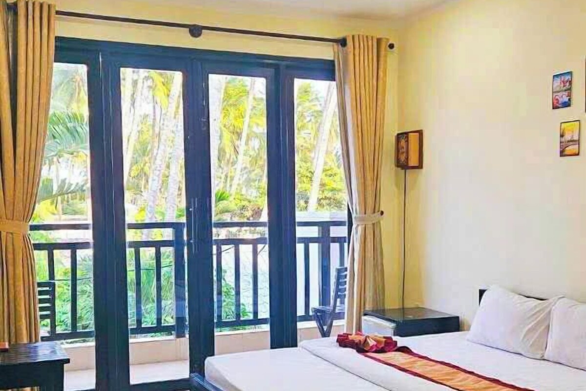 A hotel room with a bed, a desk, and a view of the outdoors through large sliding doors.