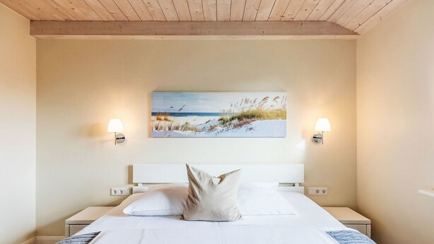 Een slaapkamer met een groot bed, twee bedlampen, een schilderij van een strand en een houten plafond.