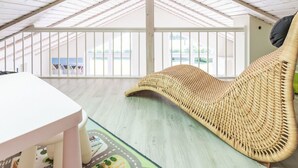 A spacious attic room with a high ceiling, a large wicker chair, and a view of houses through the windows. - Luv & Lee by Interhome (Dagebüll)