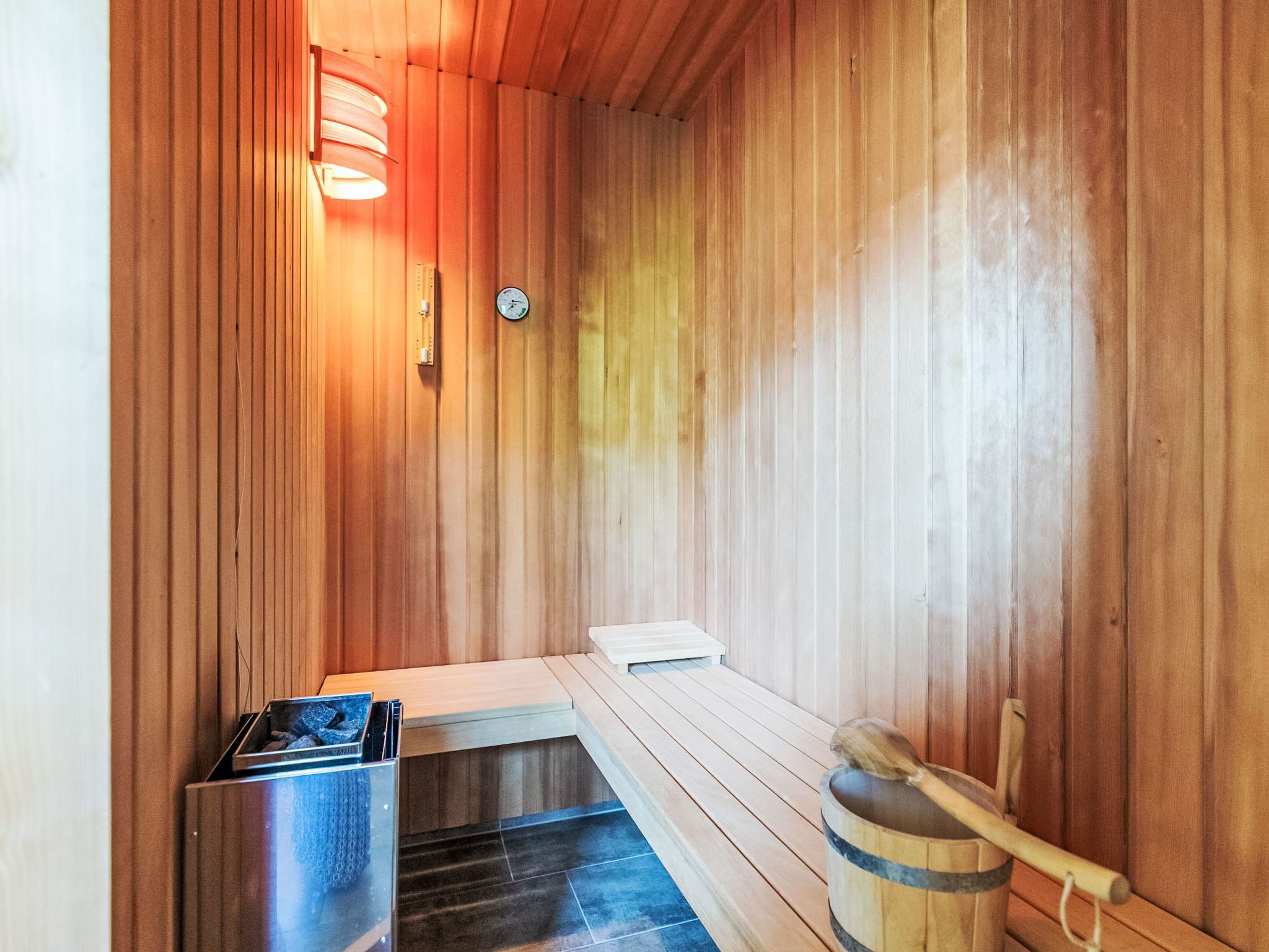 A sauna with wooden walls, a bench, a bench seat, a wooden bucket, and a thermometer.
