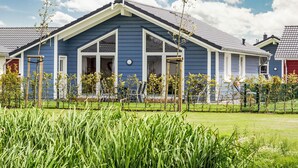 A blue house with a gabled roof, large windows, and a fenced yard with green grass and trees. - Luv & Lee by Interhome (Dagebüll)