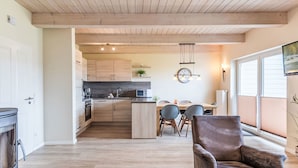 A modern kitchen with wooden cabinets, a dining area with a table and chairs, and a cozy seating area with a leather chair. - Nordseeluft by Interhome (Dagebüll)