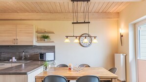 A modern kitchen with wooden cabinets, a built-in oven, and a dining area with a wooden table and four chairs. - Nordseeluft by Interhome (Dagebüll)