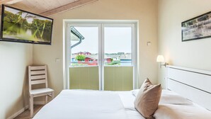 A hotel room with a bed, a chair, a TV, and a window with a view of houses. - Nordseeluft by Interhome (Dagebüll)
