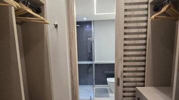 Un vestidor con estanterías abiertas, una puerta corredera que da al baño y un panel divisor de listones de madera.