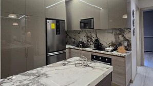 A modern kitchen with a marble countertop, stainless steel appliances, and a pendant light. - Departamento de lujo Quito Le Parc -1002 (Quito)