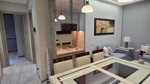 A modern dining area with a glass-top table, pendant lighting, and a view into the kitchen. - Departamento de lujo Quito Le Parc -1002 (Quito)
