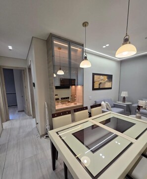A modern kitchen with a glass-top dining table, pendant lighting, and a view into the adjacent living area. - Departamento de lujo Quito Le Parc -1002 (Quito)