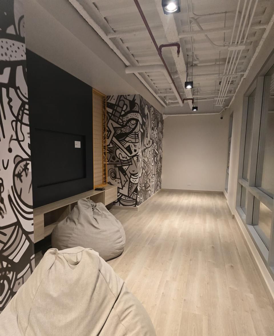 A room with a wooden floor, a black and white abstract mural on the wall, and a large window on the right.