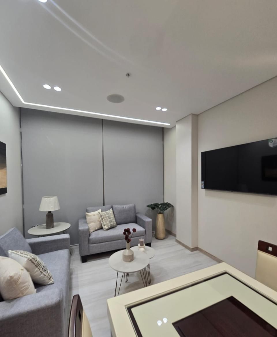Un salon moderne avec un canapé gris, une petite table ronde et un téléviseur à écran plat fixé au mur.