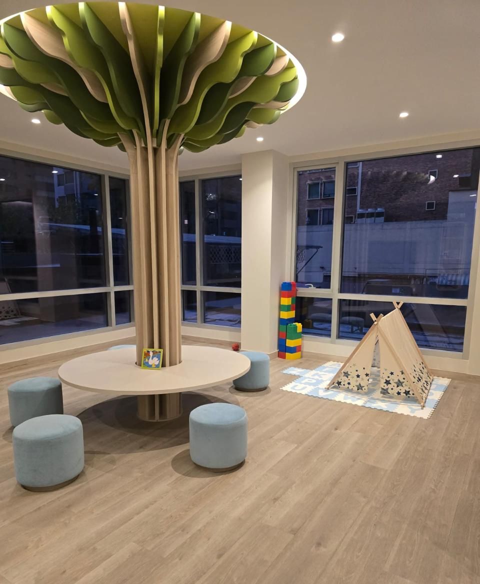 Un área de juegos para niños con una gran lámpara con forma de árbol, asientos redondos y una tienda de campaña.
