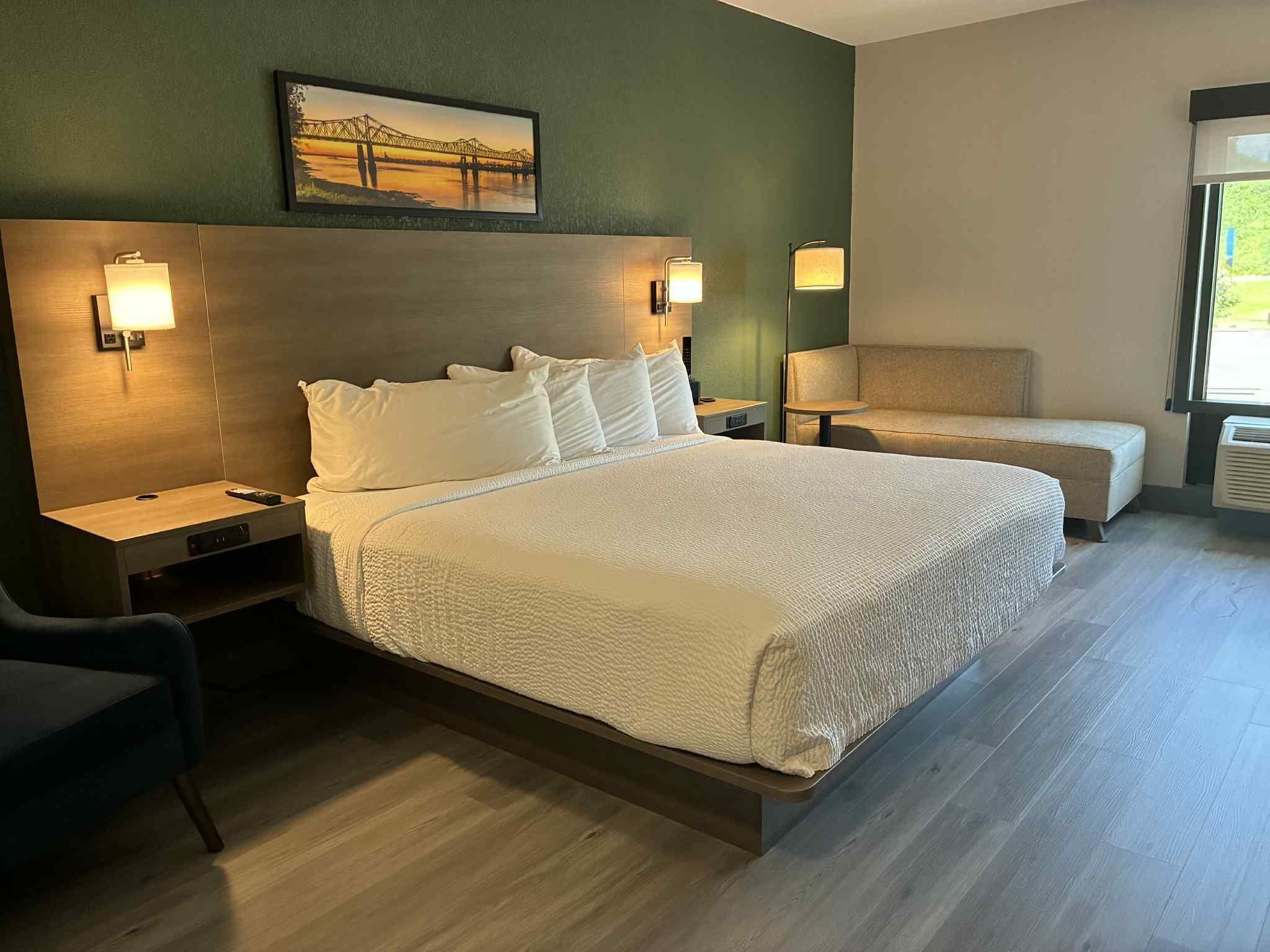 Ein Hotelzimmer mit einem großen Bett, zwei Nachttischen, einem Sessel und einem Bild an der Wand.
