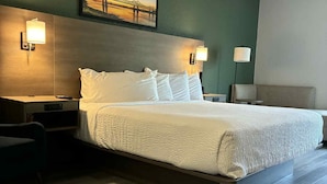A modern hotel room with a large bed, two bedside tables, a nightstand, a desk, and a chair. - The Bridges Hotel  (Natchez)
