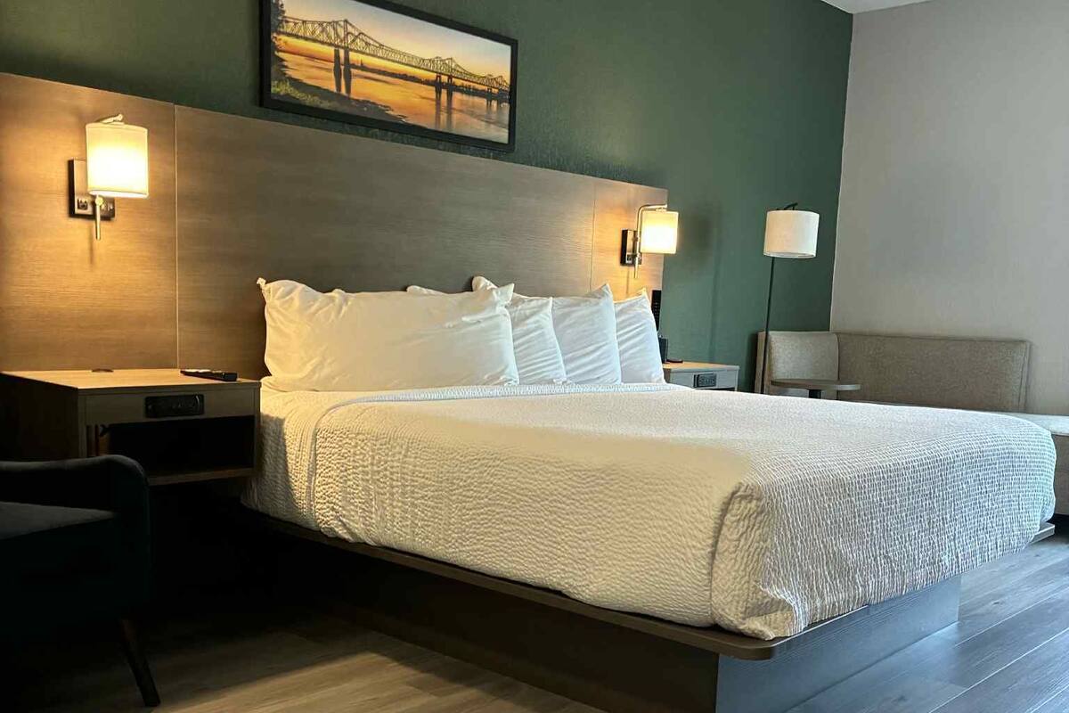 A modern hotel room with a large bed, two bedside tables, a nightstand, a desk, and a chair.