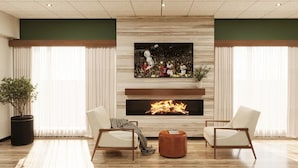 A modern living room with a fireplace, two armchairs, a coffee table, and a large window with curtains. - The Bridges Hotel  (Natchez)