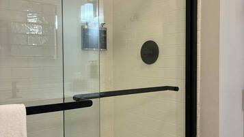 Cabina doccia in vetro con cornice nera, pareti rivestite di piastrelle bianche e un asciugamano appeso alla porta.