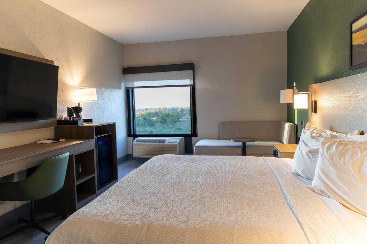 A hotel room with a bed, a desk with a chair, a TV, and a window with a view of the outdoors.